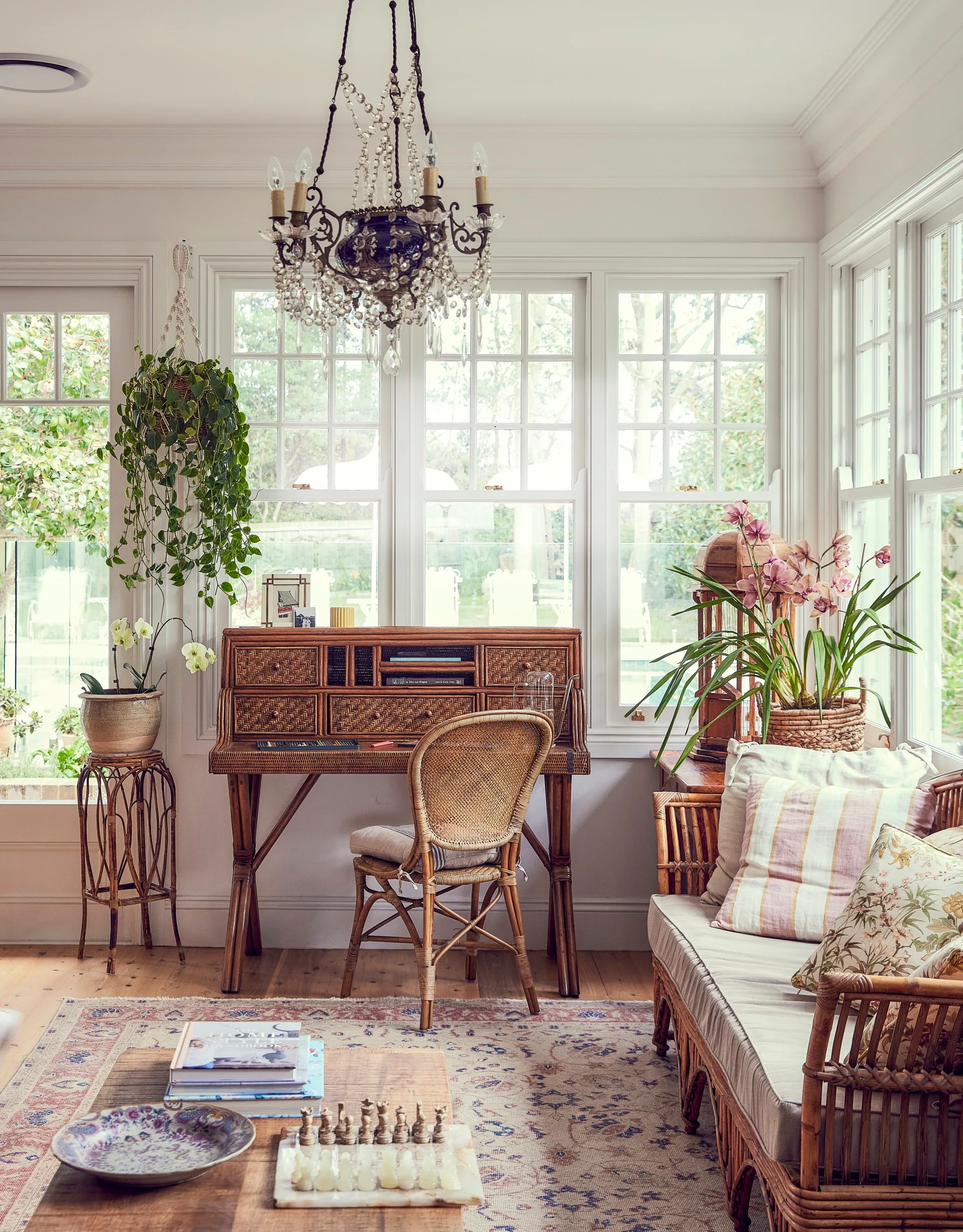 A living room with lots of natural light, rattan chair, rattan sofa and a desk with rattan drawers.