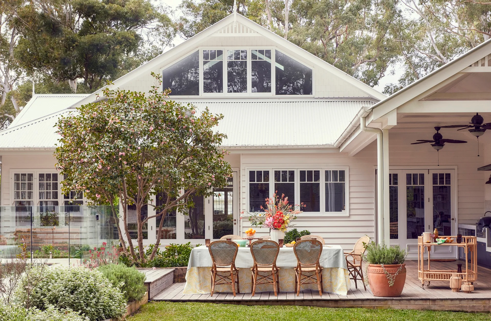 An exterior photo of a white house with an outdoor dining area with rattan styling