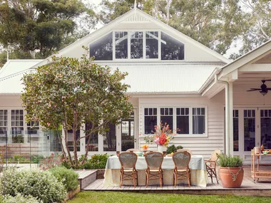 An exterior photo of a white house with an outdoor dining area with rattan styling