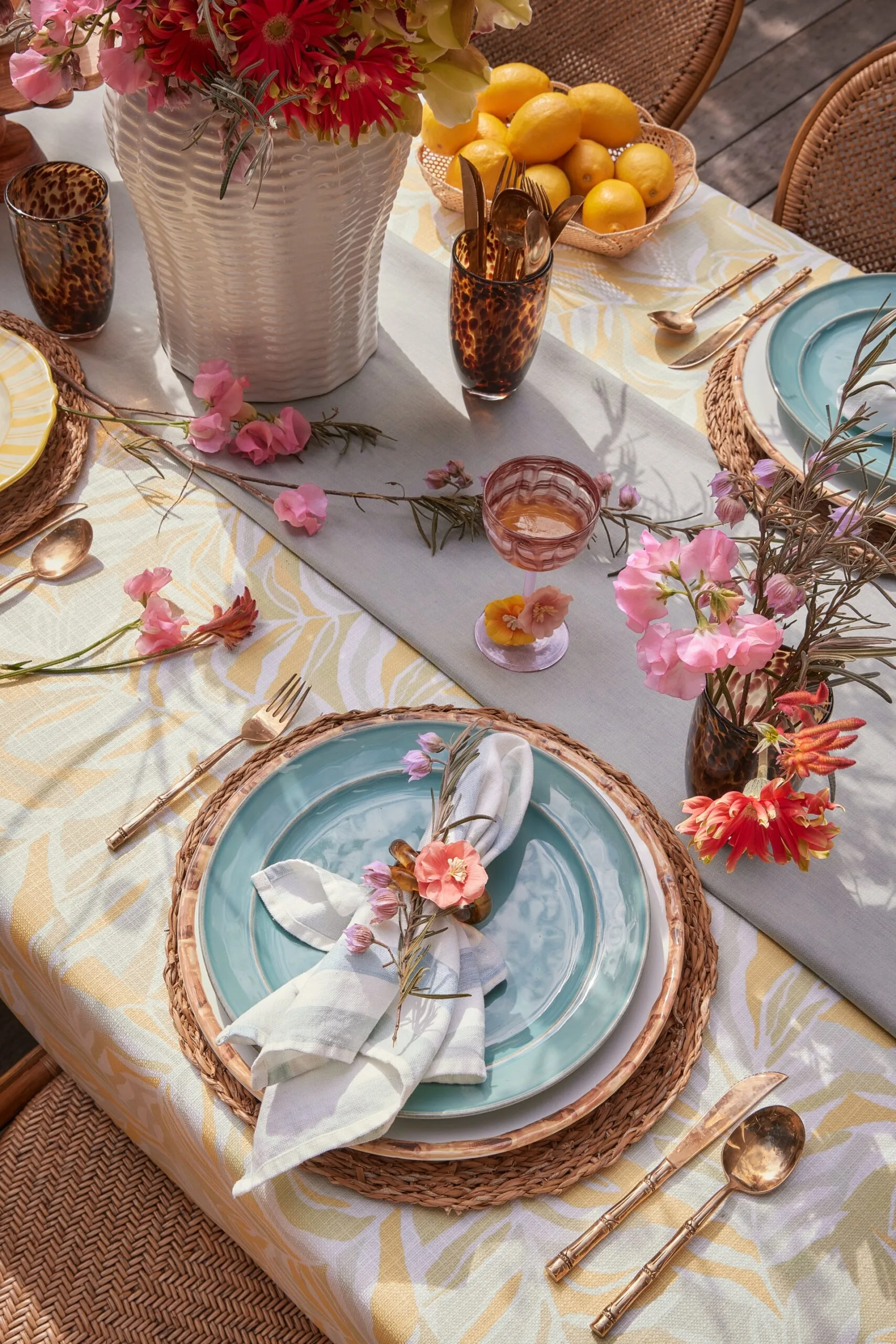 This alfresco table setting has woven placements complemented by colourful flowers.