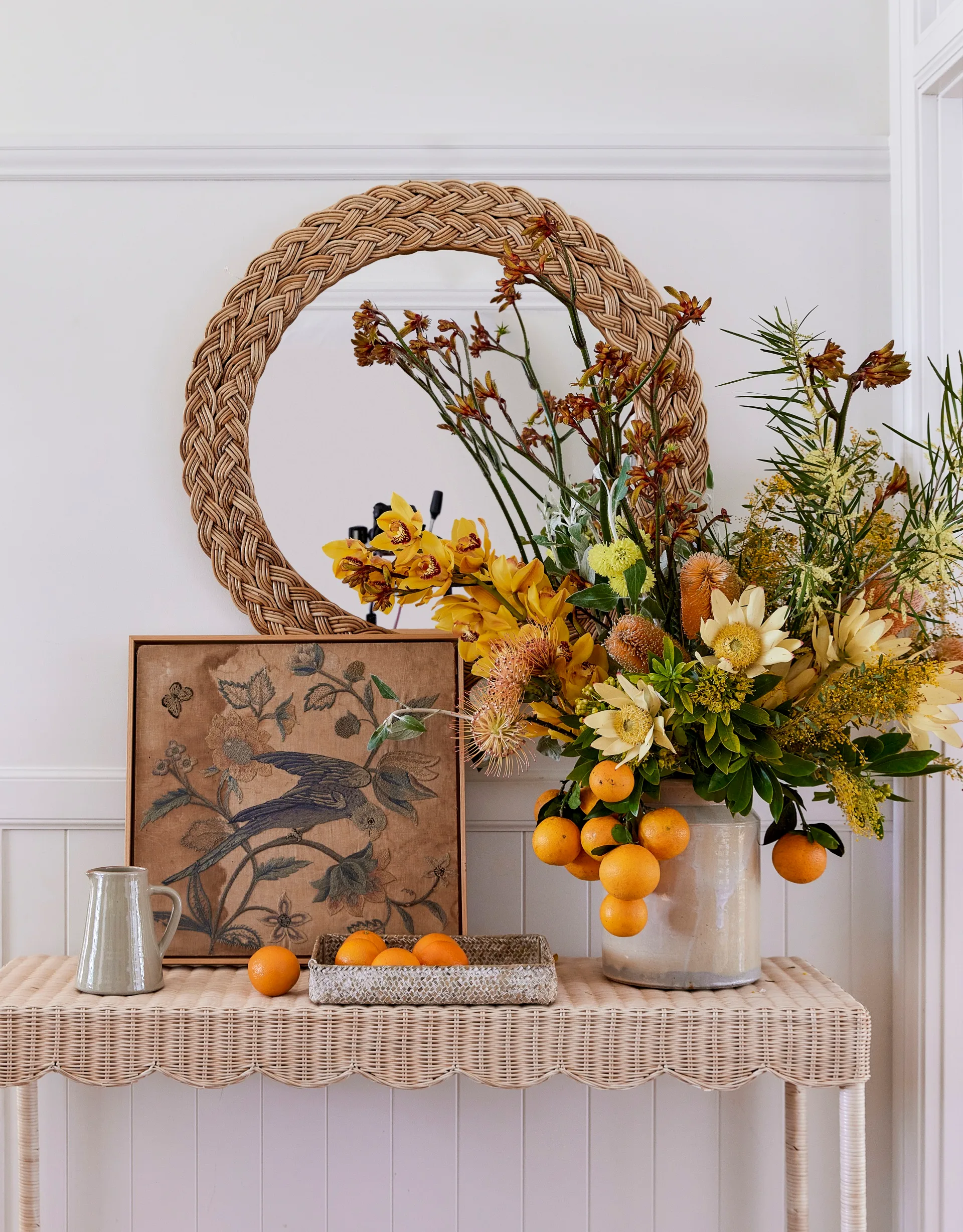 A vintage artwork of a bird is next to a vase filled with orange and yellow flowers and fruits.