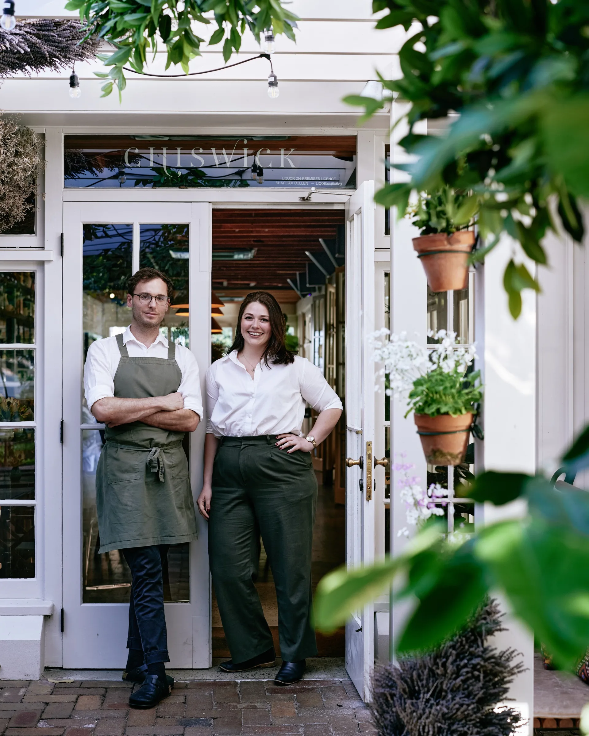 Head sommelier and head chef at Chiswick restaurant stand in the white doorway, surrounded by greenery