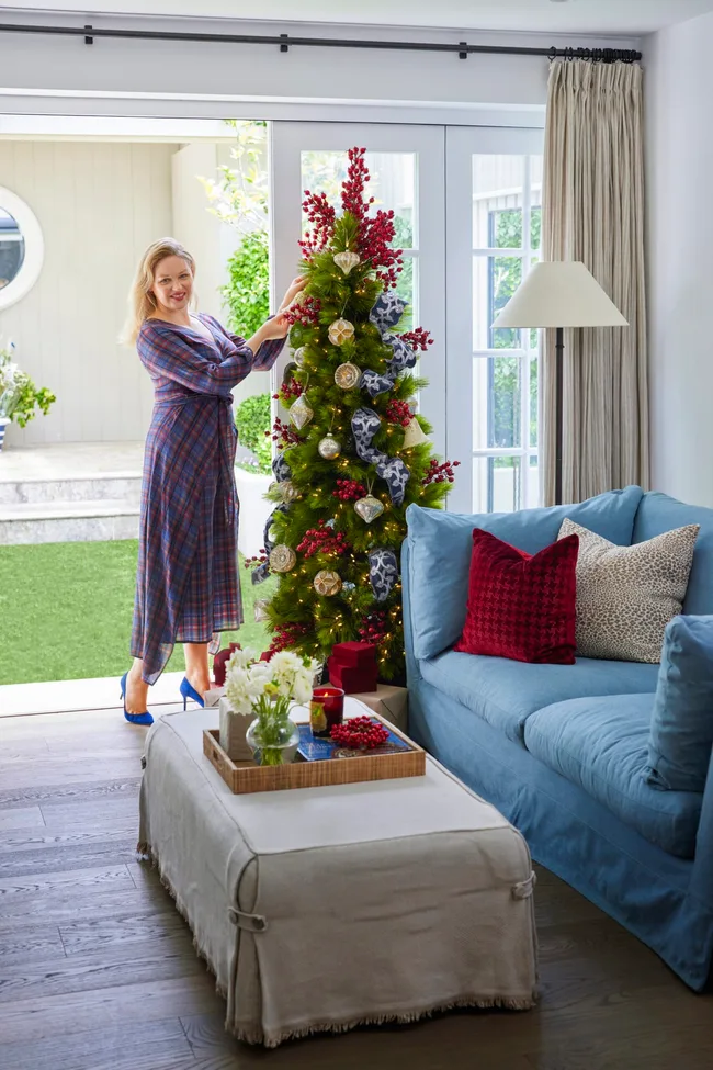 Christmas tree with blue velvet ribbon and red berries as decorations with a woman adding the finishing touches