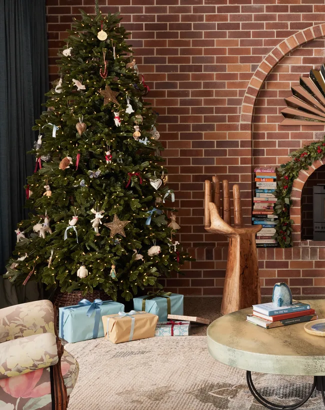 A classic Christmas tree stands in front of a warm brick wall.
