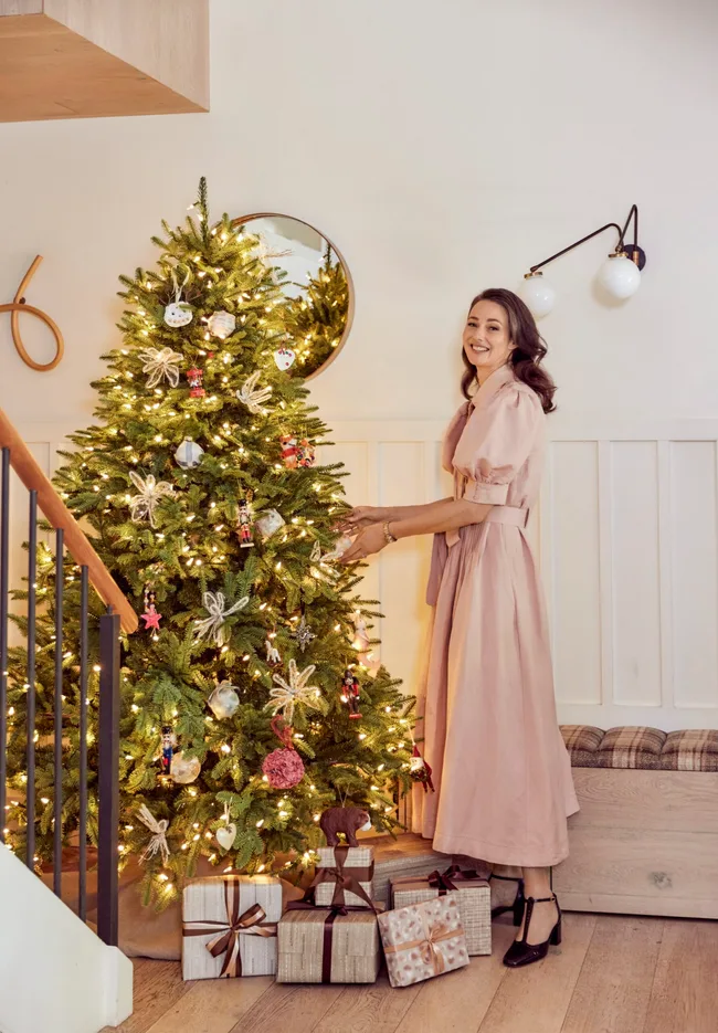 A woman spruces up her Christmas tree which has classic decorations and lots of warm white lights