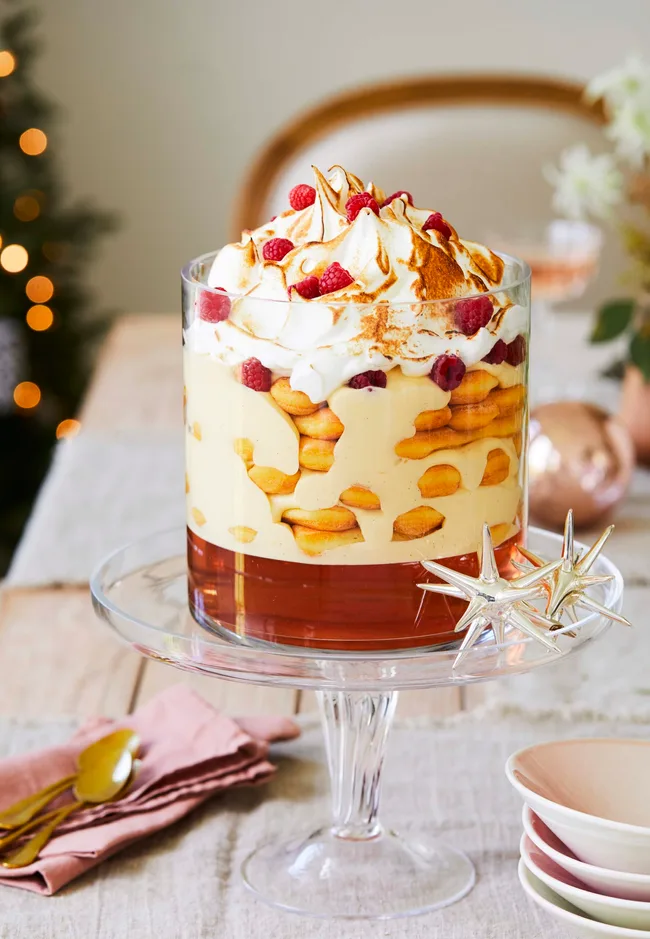 Rose and zabaglione trifle recipe served in a tall glass cylinder atop a glass cake stand with Christmas decorations