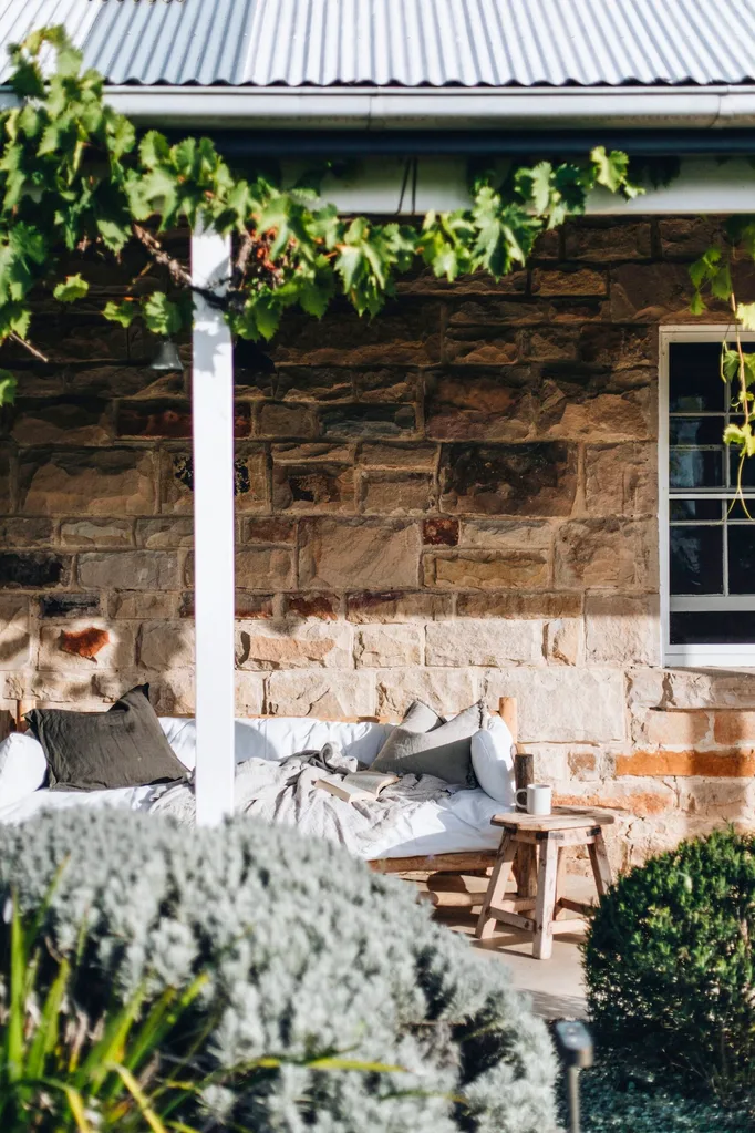 Sandstone cottage veranda with a white outdoor lounge and bushes in front
