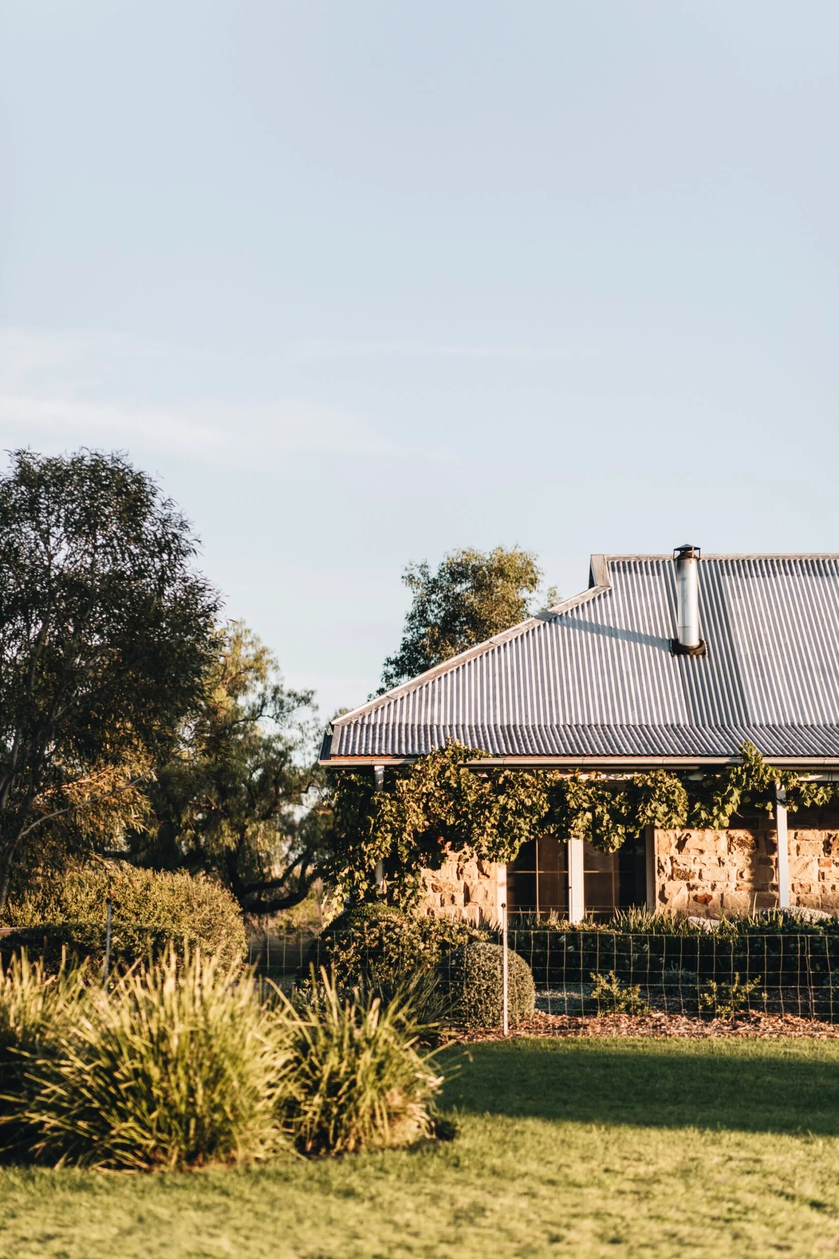 Edwina Bartholomew's sandstone cottage veranda with bushes and trees in front