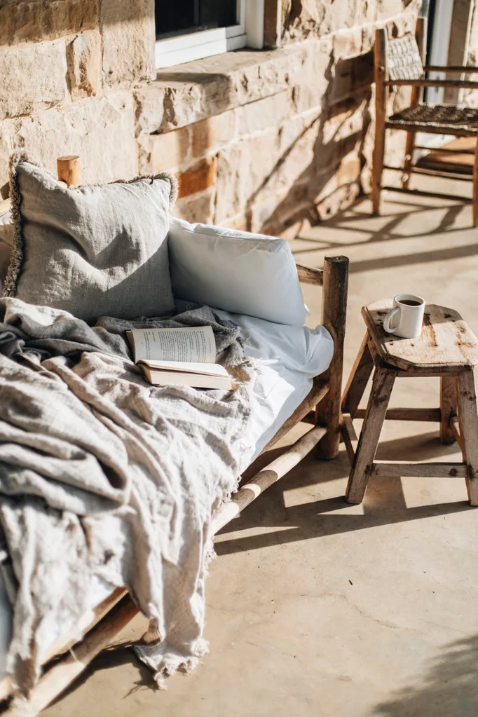 Outdoor lounge with neutral toned cushions, blankets and a wooden stool beside.