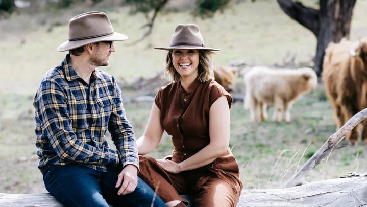 Edwina Bartholomew and Neil Varcoe on a log with pet cows in the background.