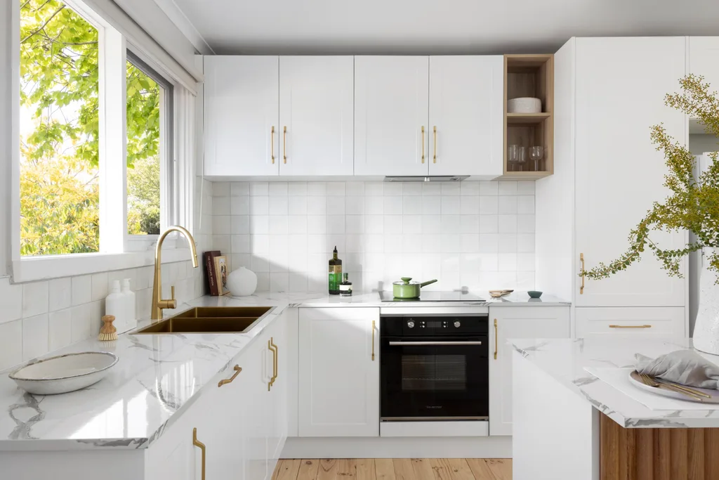 A kitchen with white cabinetry, white benchtop and white tiled splashback.