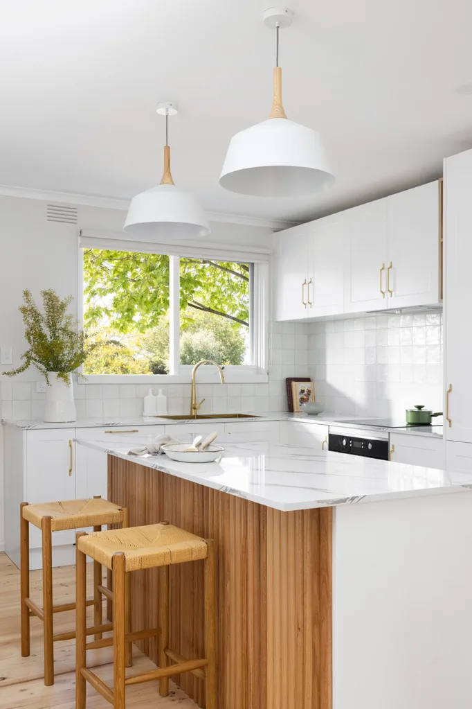 A white kitchen with timber details, including a ribbed island profile and woven bar stools.