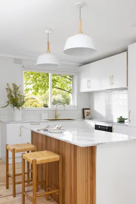 A white kitchen with timber details, including a ribbed island profile and woven bar stools.