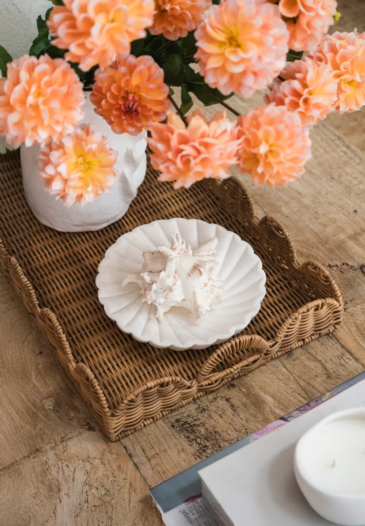 A rattan tray, white plate and white vase with orange flowers on a timber coffee table.