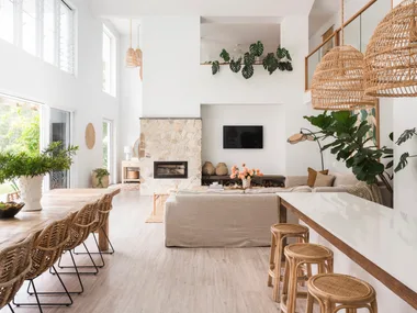 An open plan kitchen, dining and living area with mediterranean coastal style interiors, including white, reclaimed timber and a stone wall.