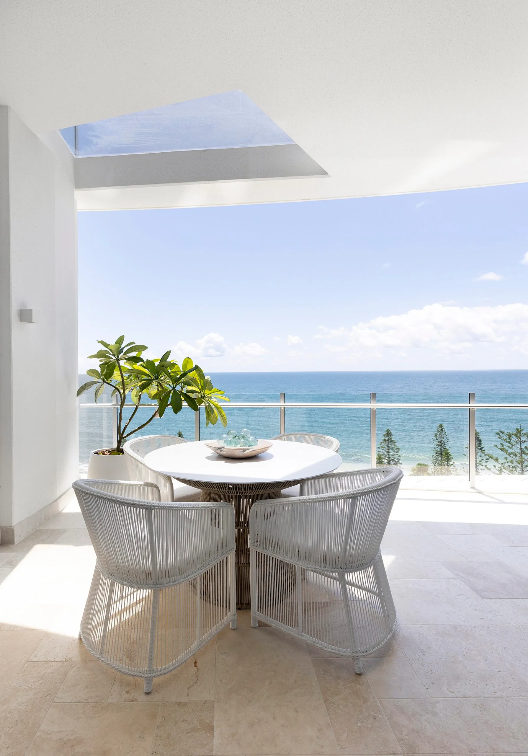 A penthouse apartment balcony with ocean views and white outdoor dining table and dining chairs.