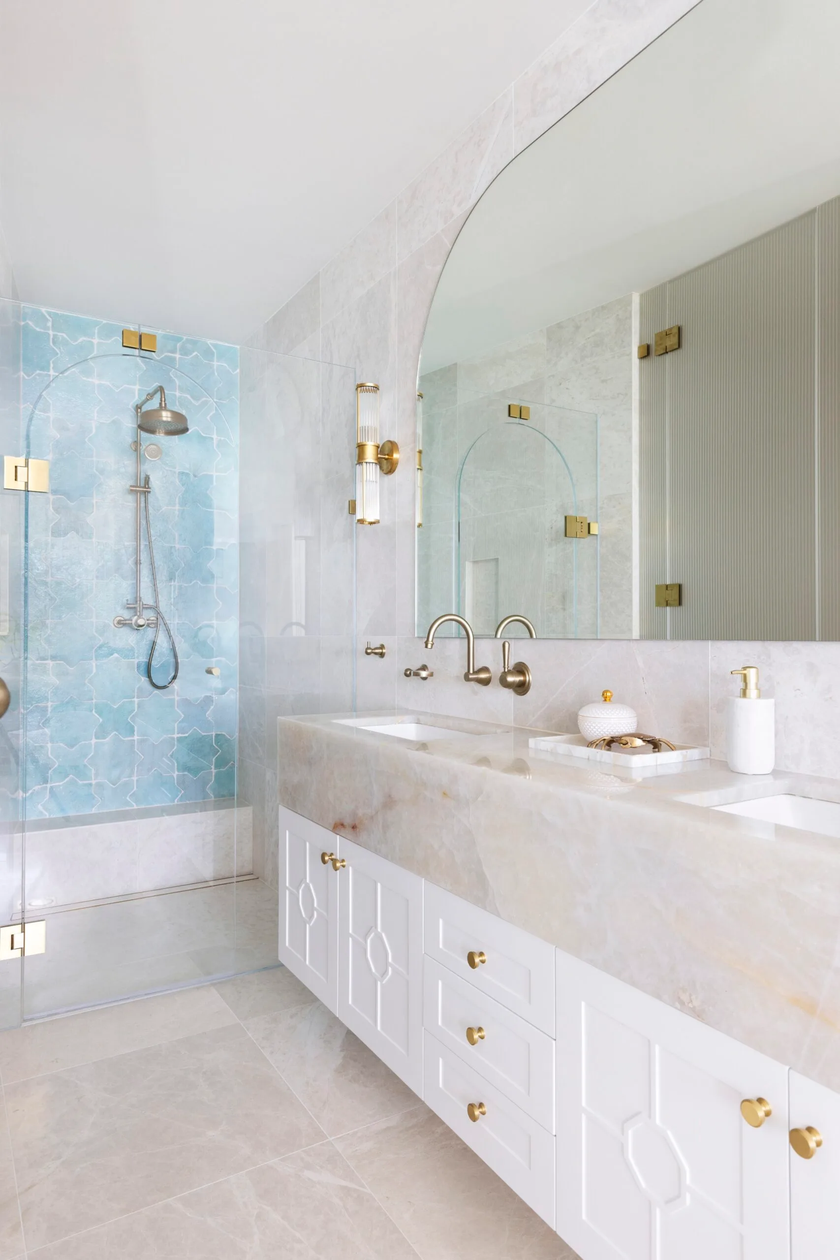 A bathroom with white cabinetry and a wall of blue tiles in the shower.