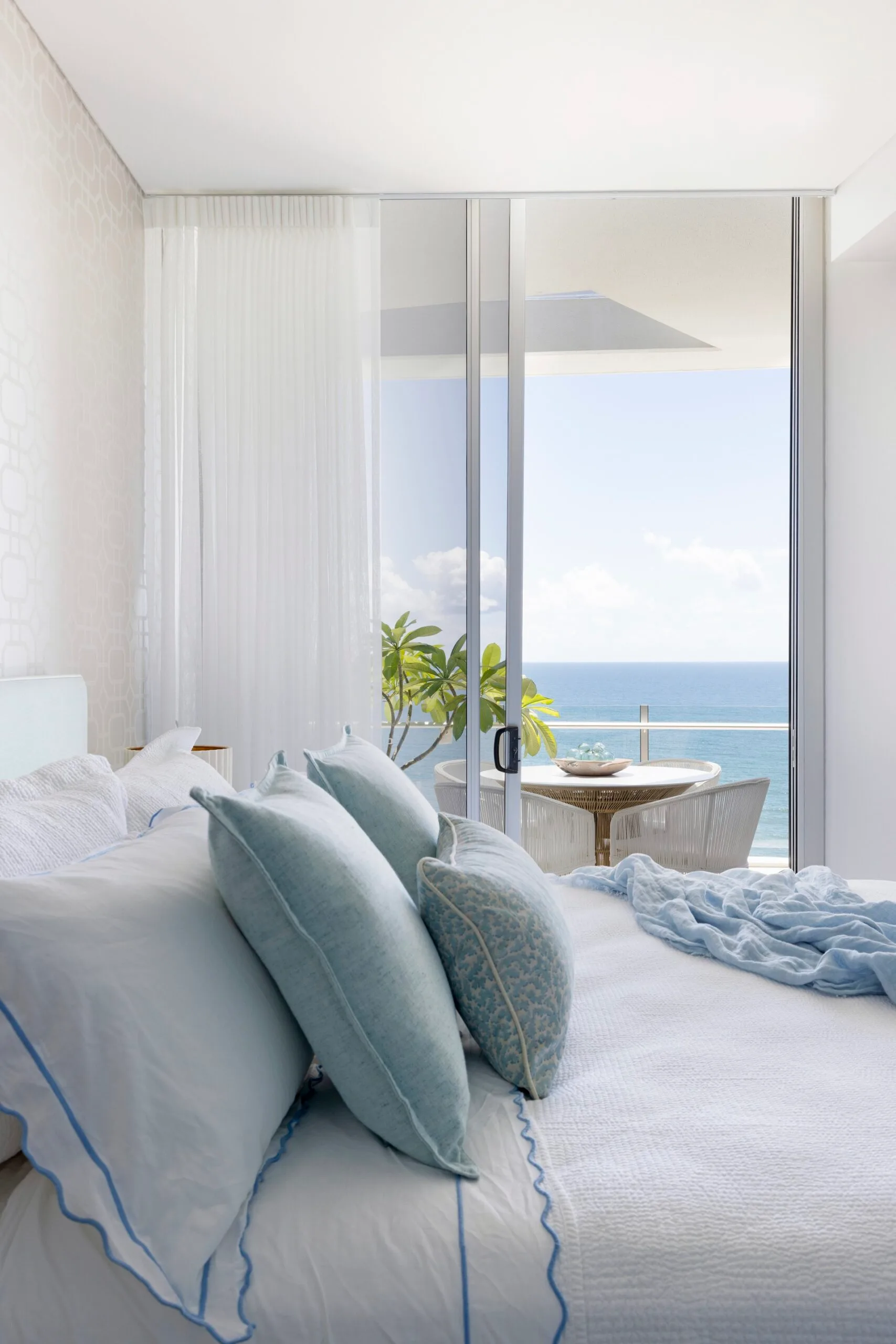 The bedroom of a penthouse apartment has ocean views and white and blue bedding to match.