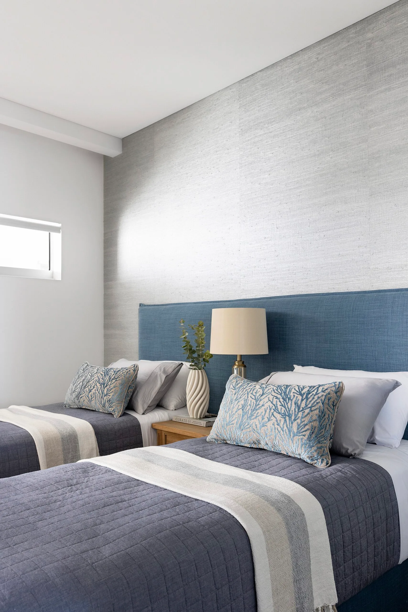 Two twin beds with blue and white bedding, with a bedside table and lamp in between.