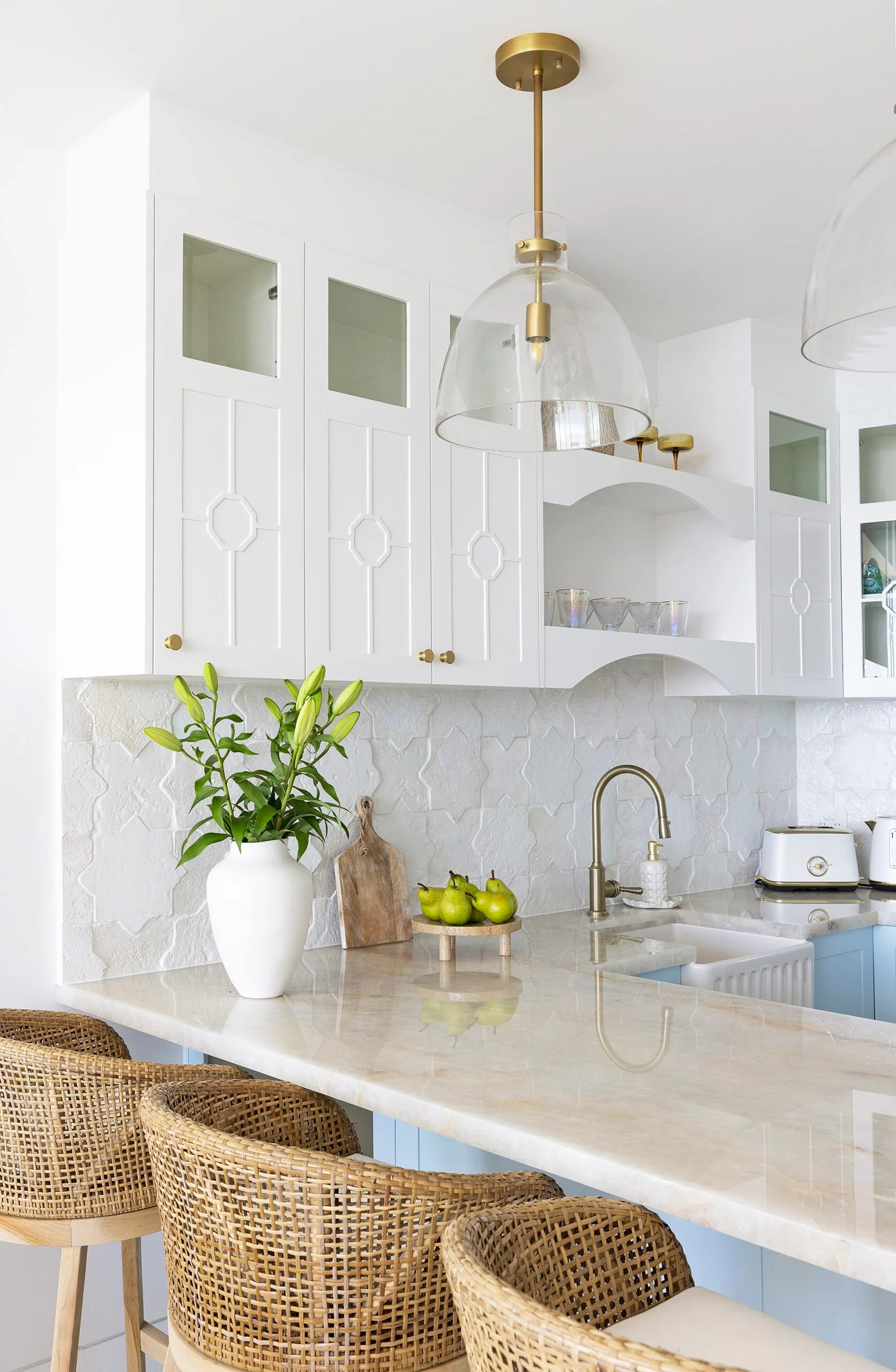 A white kitchen with rattan stools and blue cabinetry.