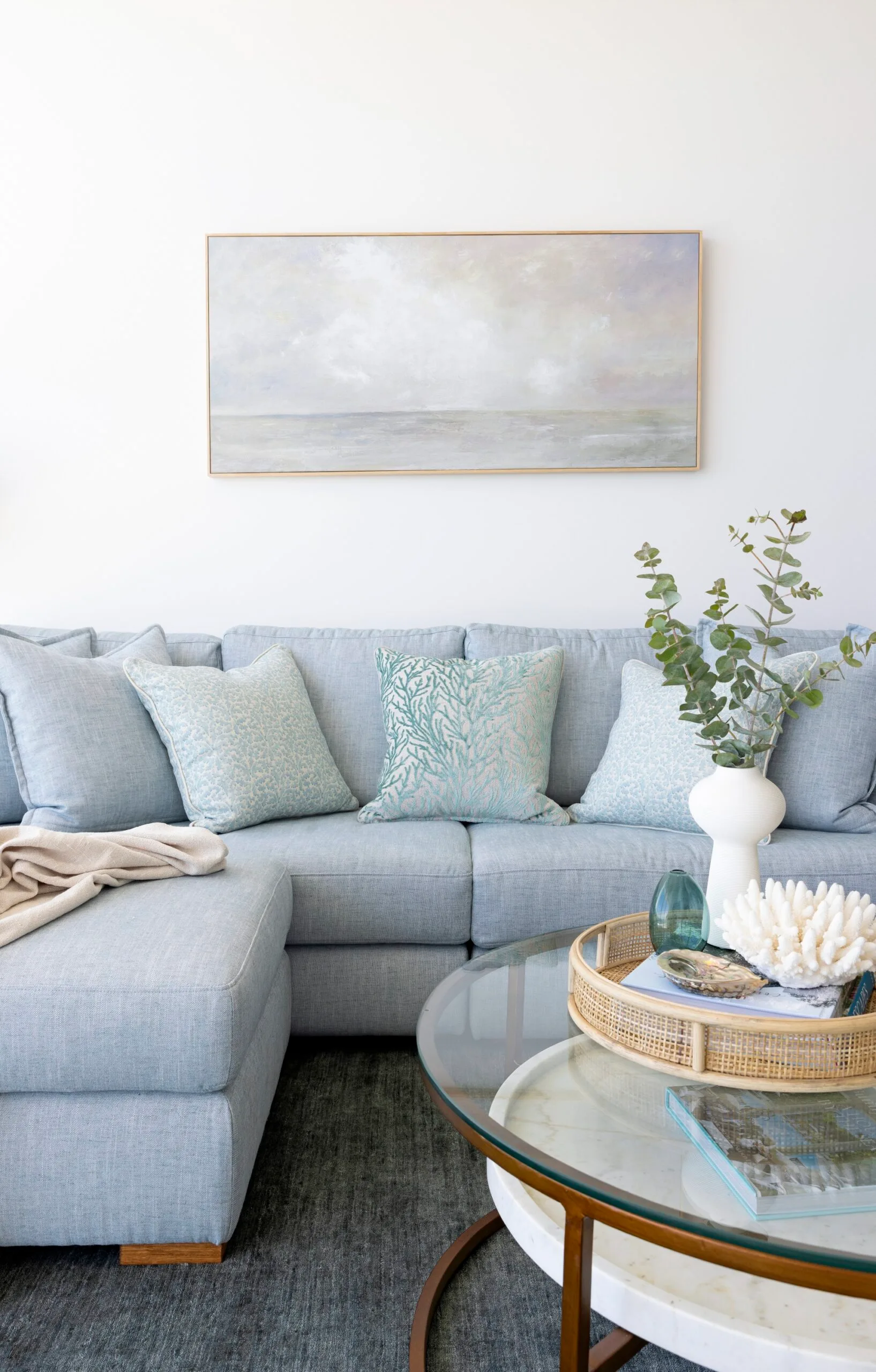 A blue sofa with a landscape painting in grey tones above it.