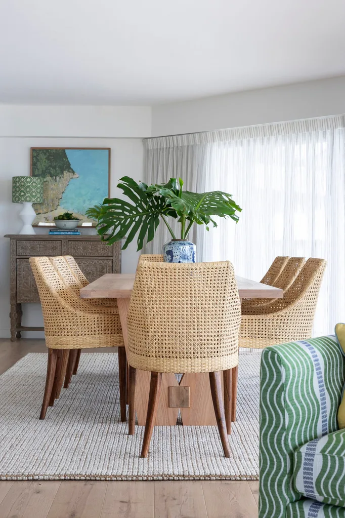 A dining table with woven dining chairs on top of a grey rug.