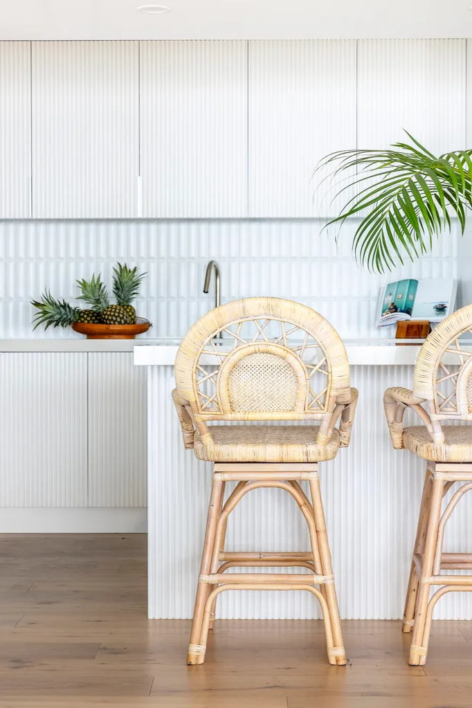 A white kitchen with a tiled splashback and woven bar stools against the kitchen bench.