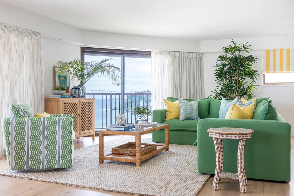 A living room with ocean views, a green sofa, blue and yellow cushions, wooden console table and coffee table.