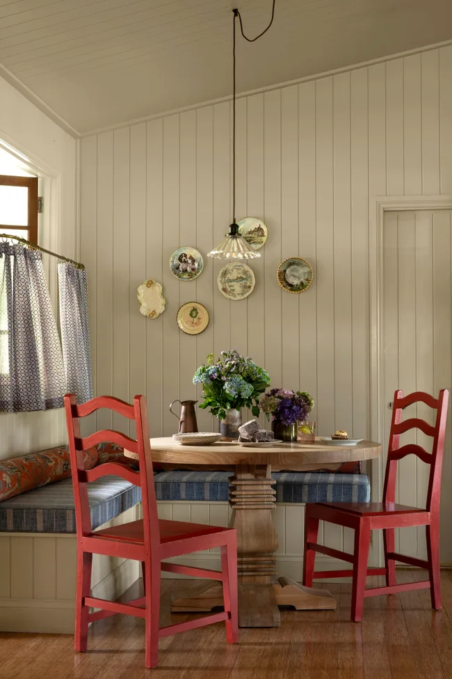 A breakfast nook with round timber table and red timber chairs in a country style modern farmhouse