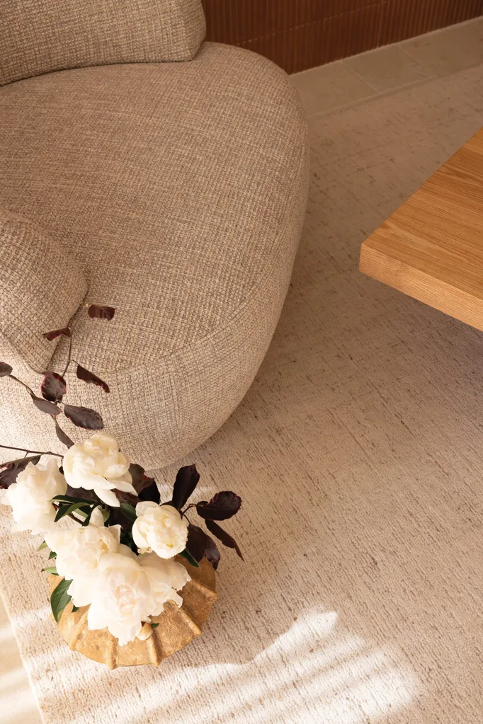 A grey armchair on top of an ivory rug with white flowers positioned beside it