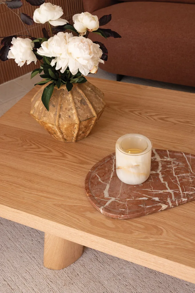 A wooden coffee table with a gold vase and white flowers on top