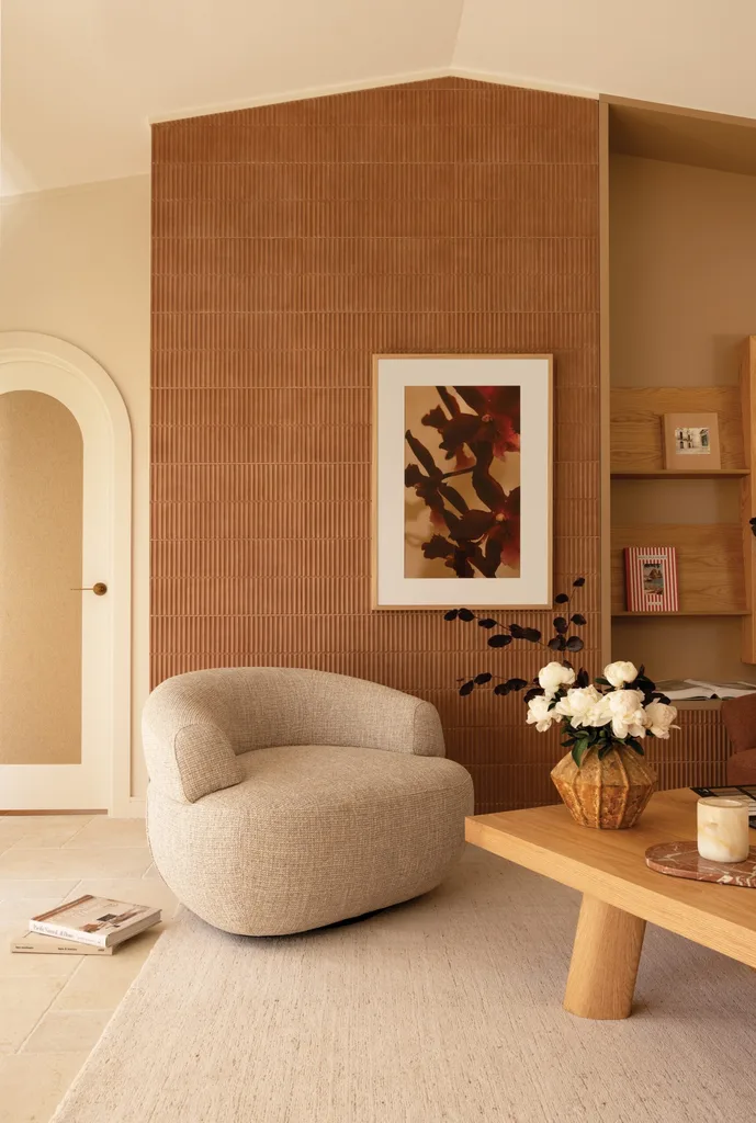 A curved armchair with a low back in grey in front of an arched white door and a wall of terracotta tiles