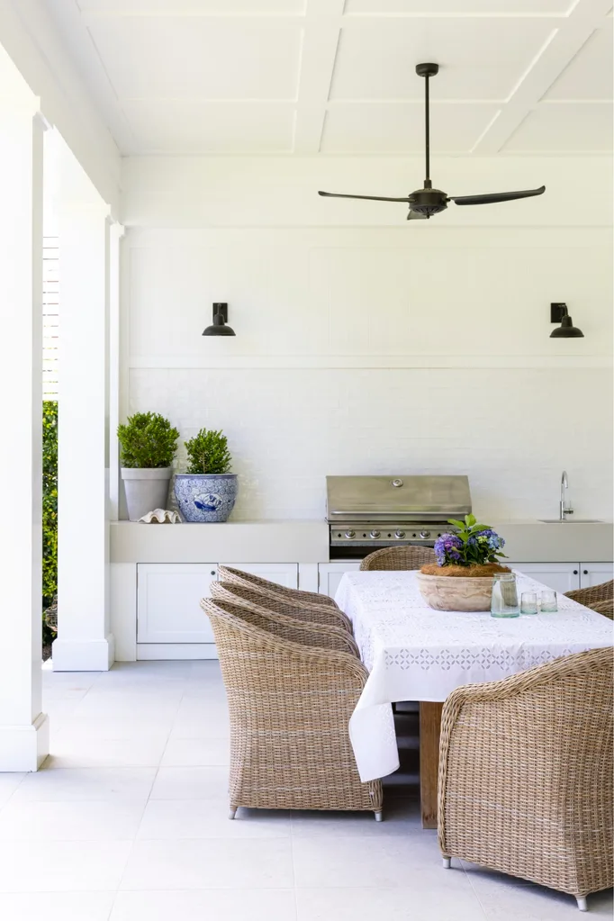 An alfresco dining area showing outdoor furniture trends with rattan chairs around a dining table with a barbecue in the background.