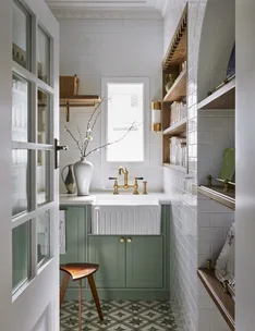A butler's pantry with white subway tiled walls, a sizable fluted fireclay sink, hardware in Satin Brass and joinery finished in a mint green colour. Timber open shelving allows owners to display trays and dinnerware, plus containers filled with ingredients. The tiled flooring has a star pattern.