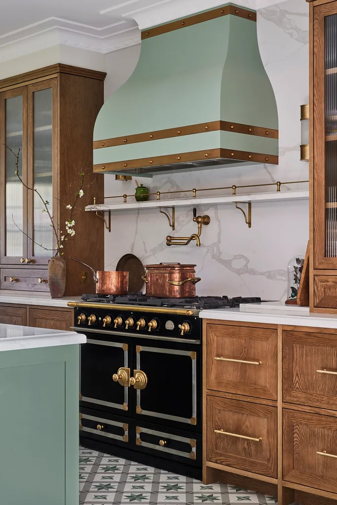 A green kitchen that was renovated with English style features to suit the 1921 build. A mint green finish is used on the kitchen island and rangehood. Wooden joinery is against the wall. Calacatta oro stone is the benchtop and splashback, which reaches all the way to the white ceiling. A La Cornue oven is opposite the island.