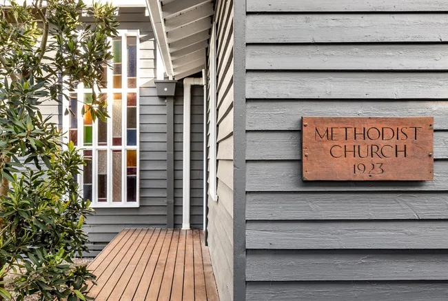 a grey weatherboard converted church with a timber deck and stained glass window