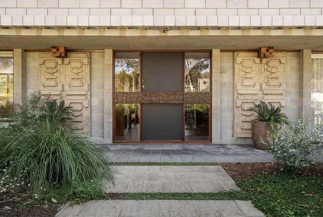 the entryway of an iconic brutalist home with concrete details and a timber front door