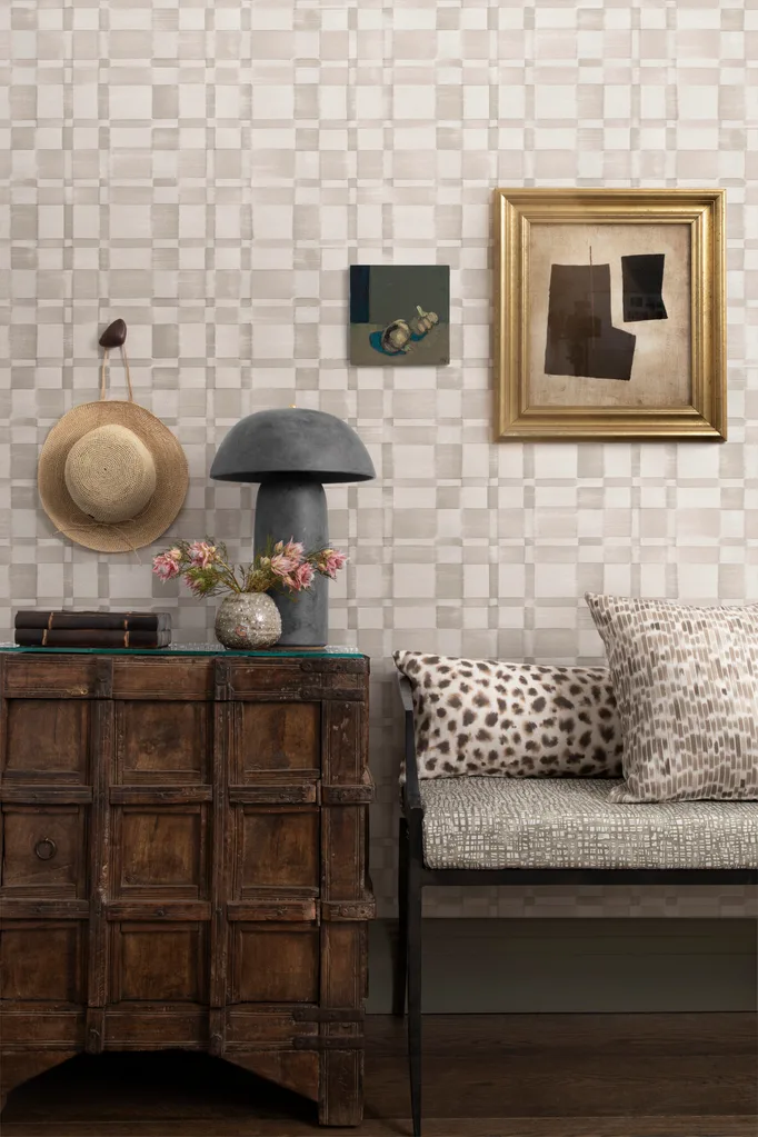 Animal print cushions on a bench with art and a lamp with wallpapered wall