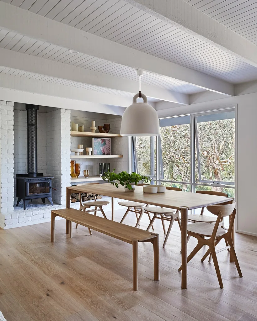 An open plan dining area with a large wooden dining table, dining chairs and bench seat on one side. A large white pendant light is suspended over the top of the dining table.