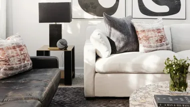 Cozy living room with a cream sofa, leather sofa, patterned cushions, a throw blanket, wicker coffee table, and decorative items.