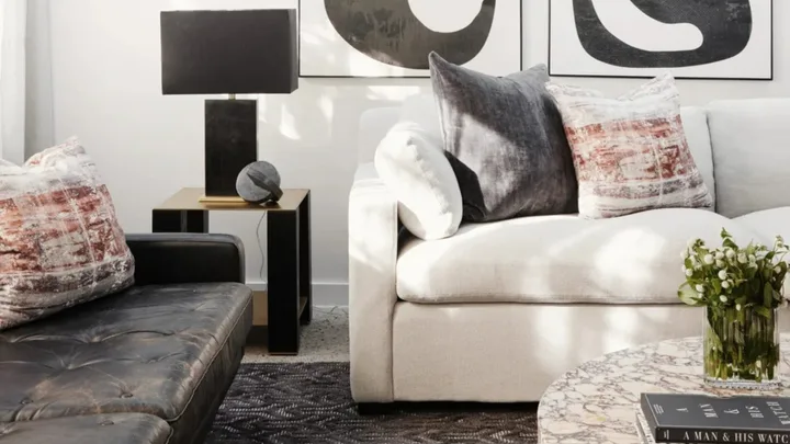 Cozy living room with a cream sofa, leather sofa, patterned cushions, a throw blanket, wicker coffee table, and decorative items.
