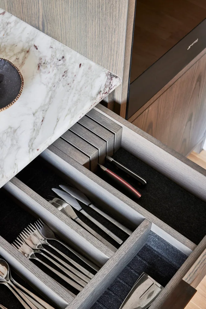 A close up photo of an open drawer which had cutlery dividers and cutlery inside. Part of the marble benchtop above the drawer is visible.