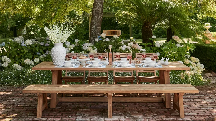 Outdoor Easter table decorating with large white vase and Easter themed place settings with white crockery on a timber outdoor dining table with timber bench seats
