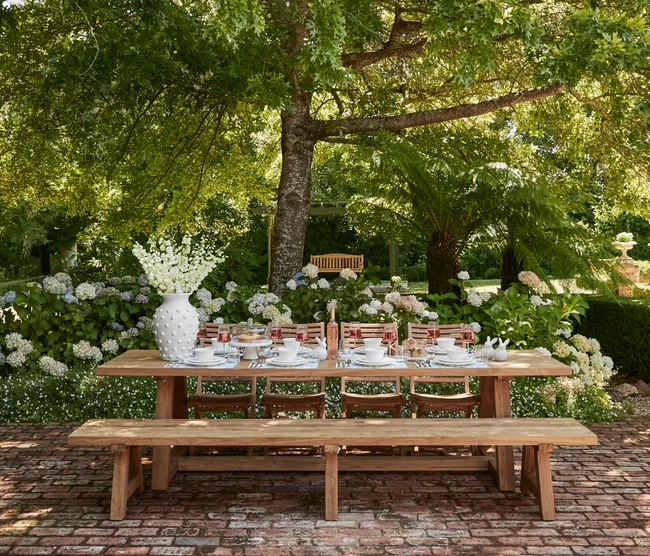 Outdoor Easter table decorating with large white vase and Easter themed place settings with white crockery on a timber outdoor dining table with timber bench seats
