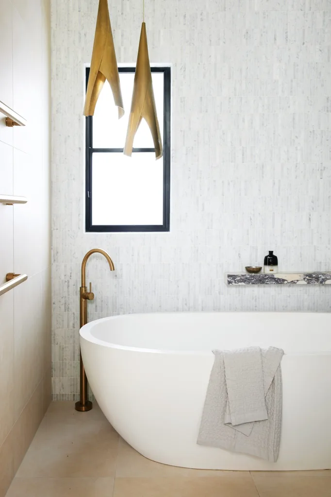 A freestanding white bathtub with brass tapware alongside and a grey towel draped over the side. The walls and floors are tiled.