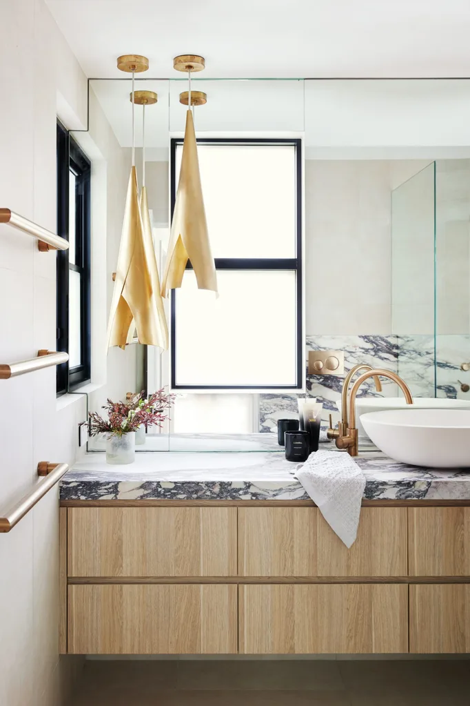 A modern bathroom with timber joinery underneath a marble benchtop, a round white basin and gold hardware.
