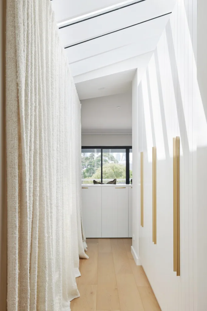 A white hallway with vaulted ceilings and skylights. One side of the hallway is lined with cream coloured curtains