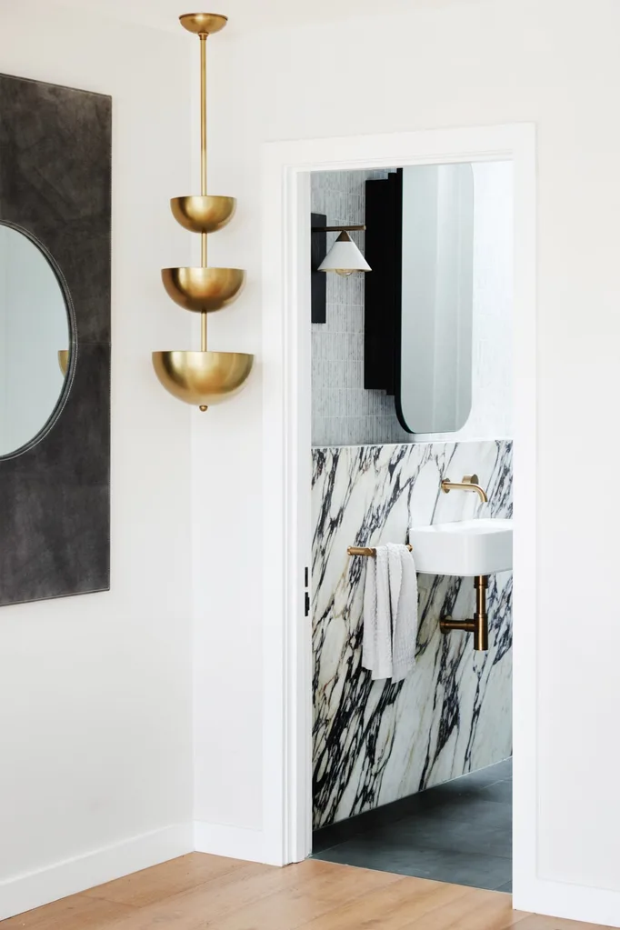 The corner of a modern style room that leads into a bathroom, with white light fittings, plus black and white marble on the wall