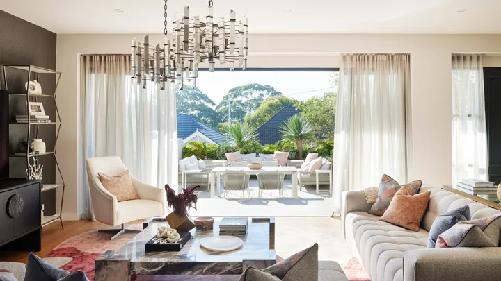 An open plan living room with a grey couch, marble coffee table and one wall painted white and one wall painted black. The sliding door opens to an outdoor living area.