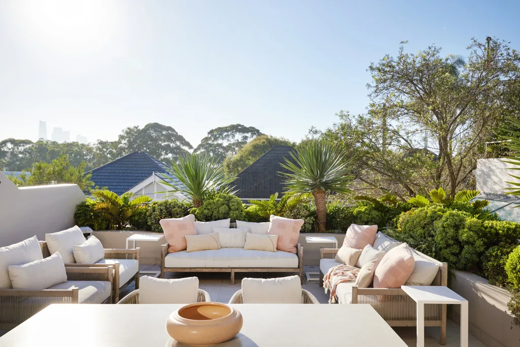 A rooftop terrace with cream toned outdoor lounges, soft pink cushions and white side tables
